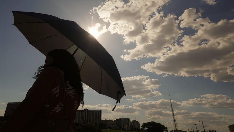 Imagem colorida mostra mulher segurando guarda-sol em dia de calor em São Paulo - Metrópoles