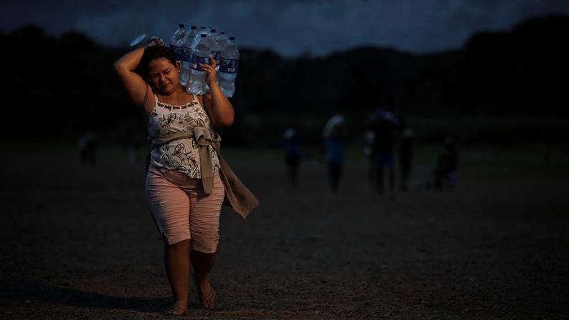Mulher carrega garrafões de água em terreno árido no Brasil durante uma onda de calor