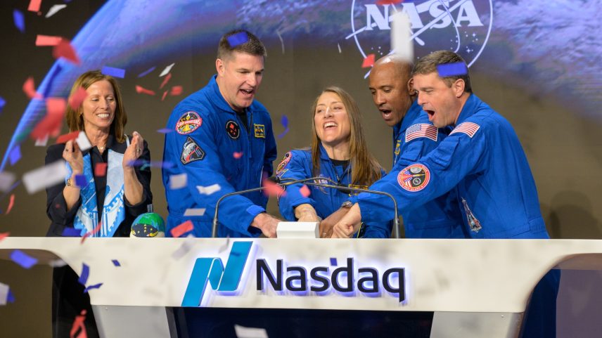 Nasdaq Chair and Chief Executive Officer Adena T. Friedman, left, and NASA’s Artemis II crewmembers CSA (Canadian Space Agency) astronaut Jeremy Hansen, and NASA astronauts Christina Koch, Victor Glover, and Reid Wiseman, right, ring the closing bell of the Nasdaq market session. They're standing behind a wide white podium with the Nasdaq logo and the word "Nasdaq." There is a screen on the front of the podium displaying the NASA meatball logo. Friedman is standing a little further away from the podium. Red, white, and blue confetti falls from the air on the left side of the image.