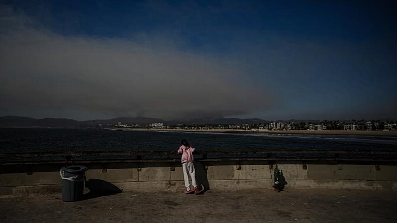 A child watches from the Venice Pier as smoke rises from the Palisades wildfires in the background on 11 January 2025 in Los Angeles, California.