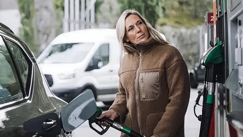Getty Images A stock photo of lady in a brown jacket filling up her car with fuel at a petrol station.