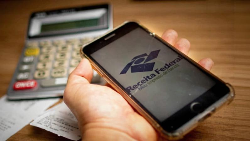 mão segura celular que acessa app do Imposto de renda - Metrópoles