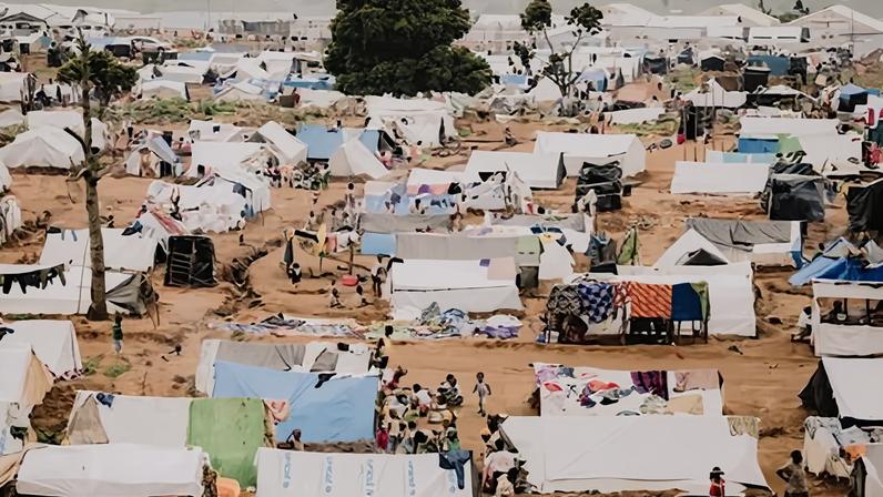 A view of tents pitched on muddy soil, trees and people walking around