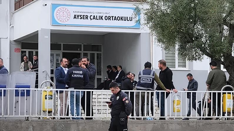 About two dozen men stand outside a school building, which has a sign reading 'Ayser Calik Ortaokulu', wearing a mix of plain civilian clothes and police uniforms.