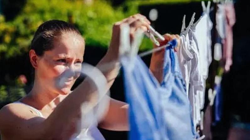 Getty Images A woman wearing a white sleeveless top smiles as she hangs out a laundry on the washing line outside.