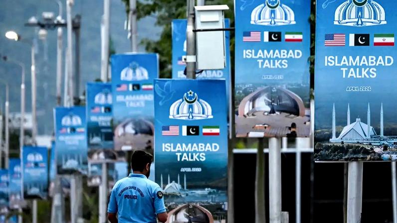 Um policial caminha ao lado de cartazes que destacam a mediação do Paquistão nas negociações de paz entre Irã e EUA, na área da Zona Vermelha em Islamabad, em 18 de abril de 2026