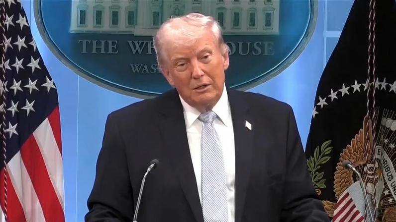 Trump entre bandeiras, atrás de púlpito, dando entrevista na Casa Branca