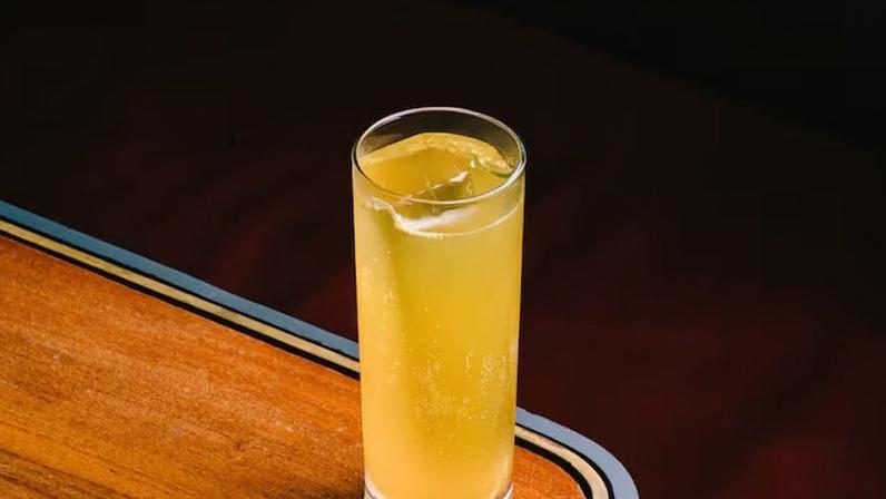 Drinque amarelo em copo de vidro em cima de mesa de madeira
