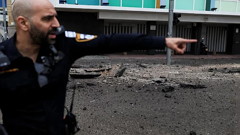 Policial israelense gesticula no local dos danos causados ​​pelo lançamento de mísseis iranianos contra Israel em Tel Aviv, Israel, em 1º de abril de 2026