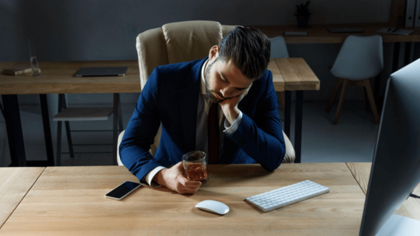 Executivo cansado segurando whisky no escritório.