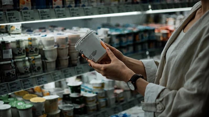 Foto colorida de mulher perto de freezer de iogurtes em supermercado - Metrópoles