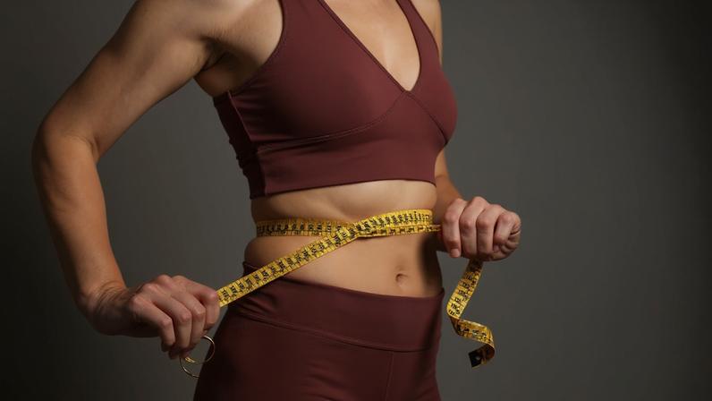 Foto colorida de mulher com fita métrica na barriga. Ela usa um cropped e uma legging - Metrópoles - emagrecer