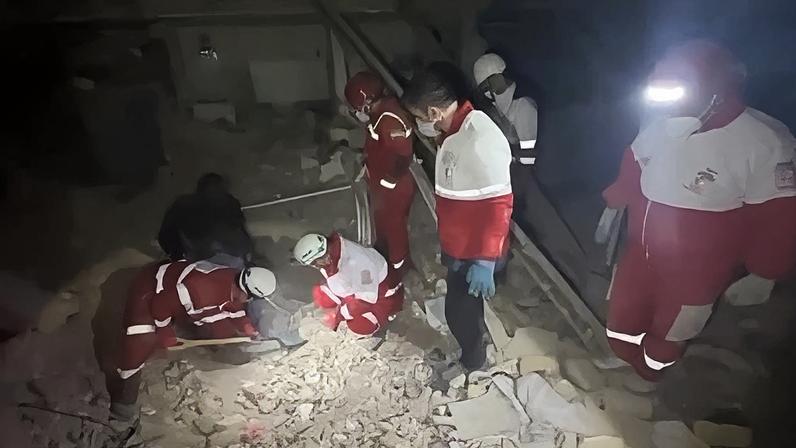 Equipes de resgate do Crescente Vermelho Iraniano vasculham escombros em área residencial de Teerã após ataque aéreo.