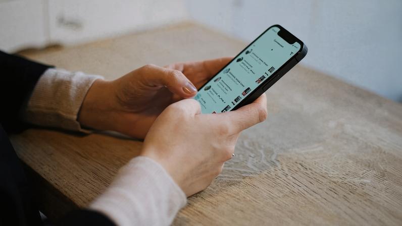 Pessoa apoiada na mesa mexendo no celular | Pexels