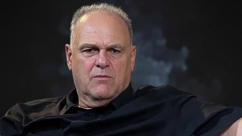 Oscar Schimidt vestindo camiseta preta sentado em sofá branco