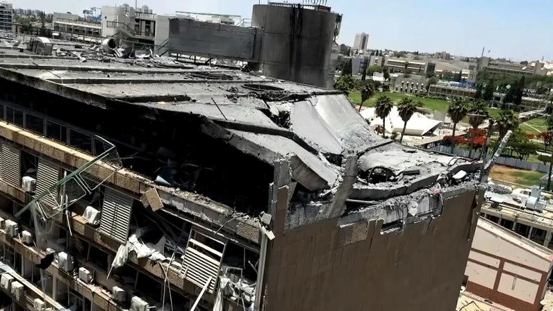 Prédio gravemente danificado, com o topo parcialmente destruído e escombros expostos. Estruturas de concreto quebradas, janelas ausentes e equipamentos pendurados