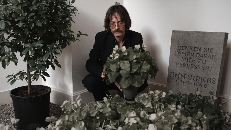 Timm Ulrichs with a gravestone commissioned by him that reads, “Always remember to forget me! Timm Ulrichs * 3.31.1940,” Kunstverein Braunschweig, September 26, 1975