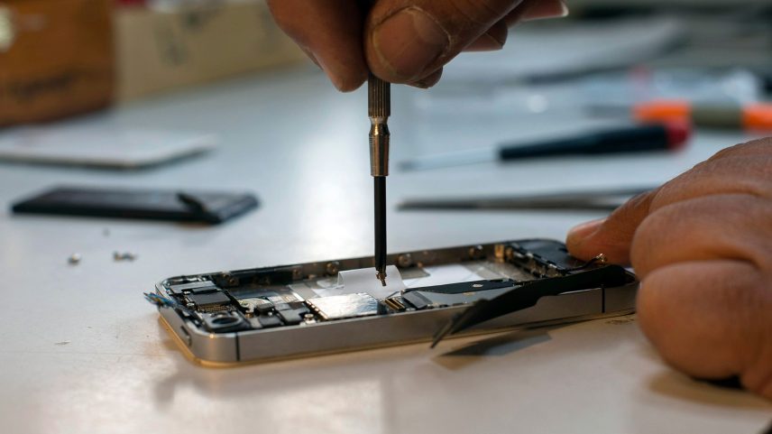A cellphone is repaired by human hands holding a screw driver