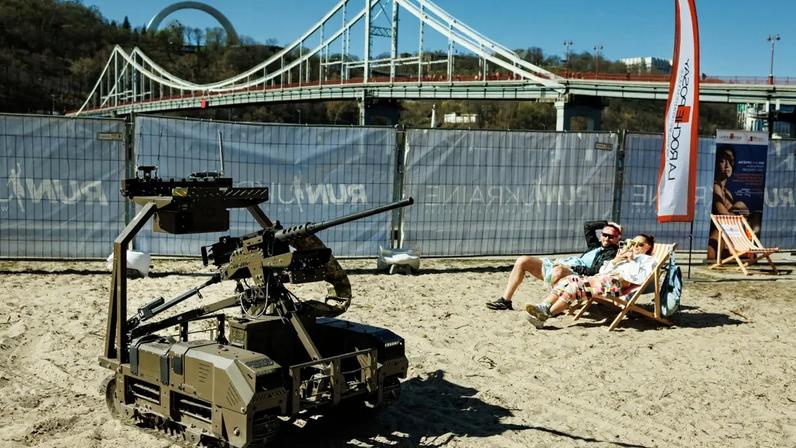 Pessoas relaxam ao lado de um veículo terrestre não tripulado exposto na Ilha de Trukhaniv, em Kiev, Ucrânia