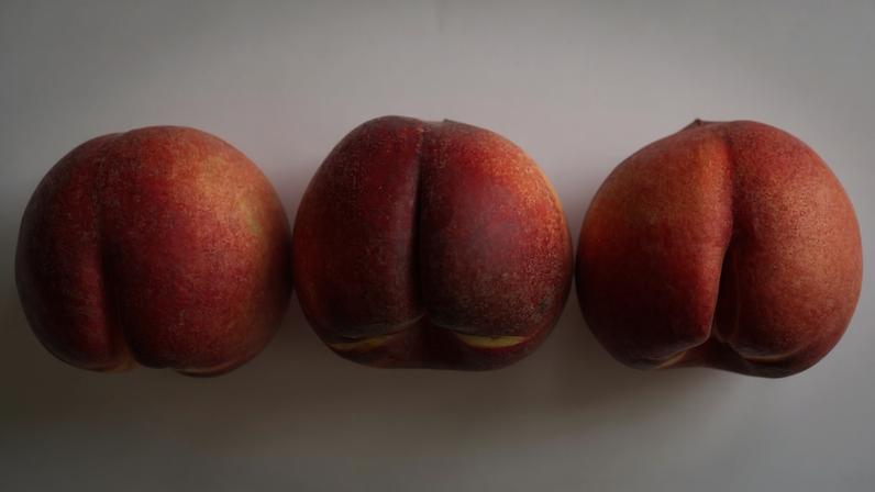 Foto colorida mostra uma fileira de pêssegos sobre uma superfície branca. Imagem faz alusão aos glúteos, bumbum, ânus