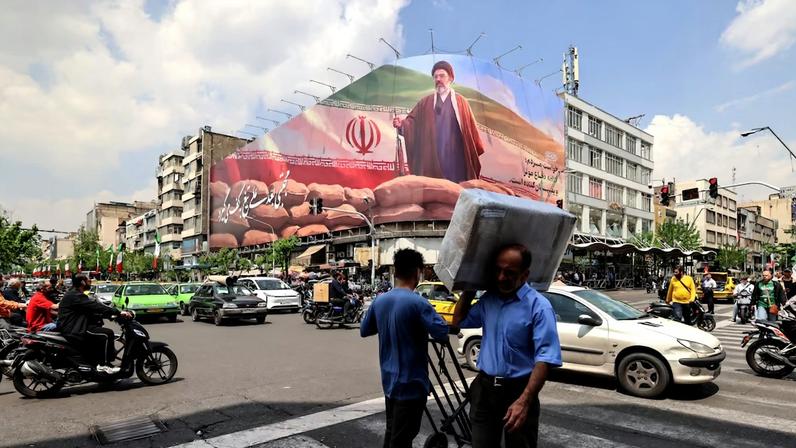 Um homem carregando um pacote no ombro passa por um grande outdoor com a imagem do Líder Supremo do Irã, o Aiatolá Mojtaba Khamenei, em uma rua de Teerã, em 20 de abril de 2026 Foto: Atta Kenare/AFP