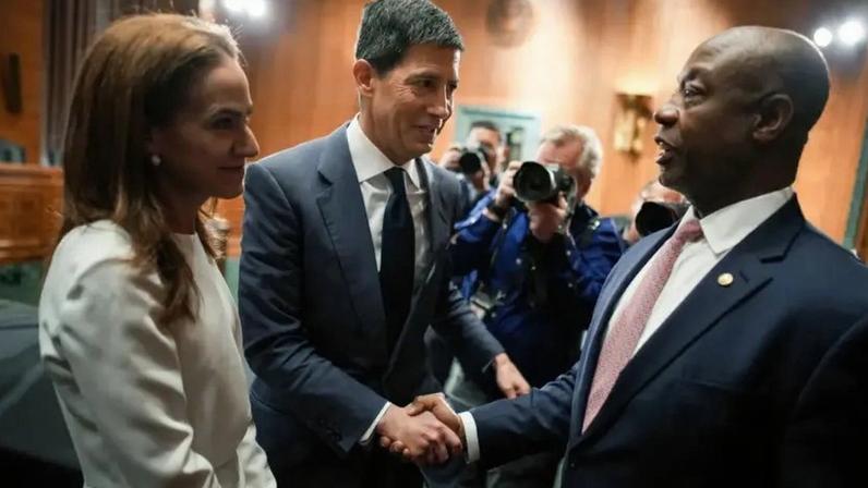 Kevin Warsh (ao centro), indicado pelo presidente Donald Trump para a presidência do Federal Reserve, e sua esposa Jane Lauder (à esquerda) cumprimentando o senador Tim Scott, presidente do Comitê Bancário, Habitacional e de Assuntos Urbanos do Senado, na audiência de confirmação de Warsh em 21 de abril de 2026, em Washington, DC