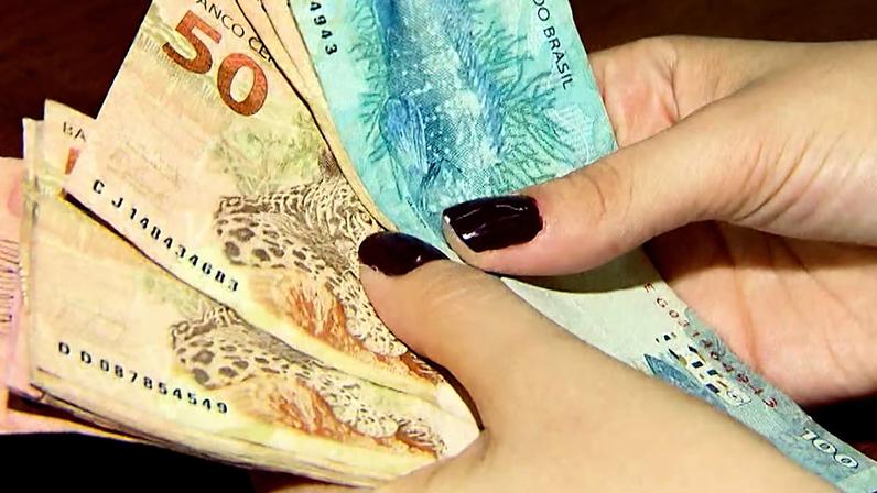 Mãos segurando notas de reais, incluindo cédulas de 50 e 100 reais