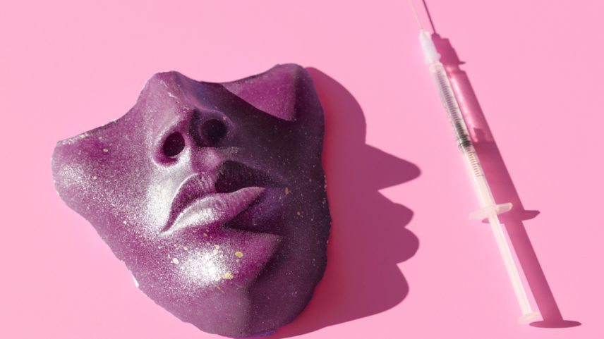 Imagem, em fundo rosa, de uma máscara ao lado de uma seringa com agulha.