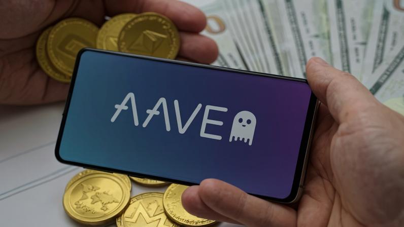 Uma mão segunra smartphone comlogomarca Aave e outra mãos critpomeodas Ethereum