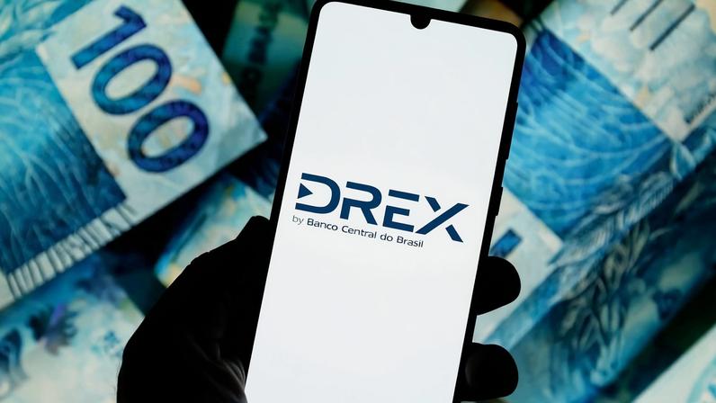 Tela de celular mostra logotipo Drex- no fundo notas de cem reais