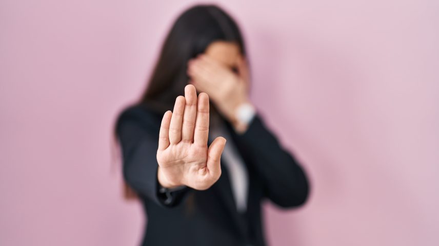 A Young brunette woman wearing business style over pink background covering eyes with hands and doing stop gesture with sad and fear expression. embarrassed and negative concept.