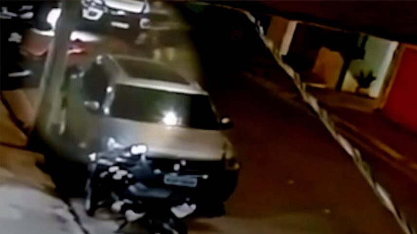 Mesmo caído, o homem ainda tenta continuar atirando. Na sequência, o filho dele aparece saindo da residência com as mãos levantadas e é abordado.