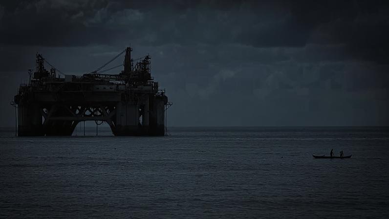 Plataforma de petróleo no mar, com um pequeno barco ao fundo sob céu nublado
