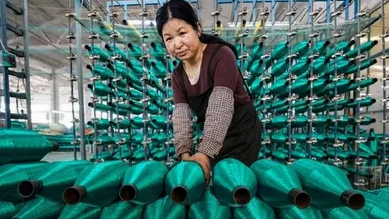 Getty Images A woman stacks rolls of bright green fishing nets on a production line at factory