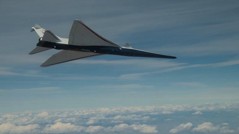 NASA's X-59 supersonic jet with blue hull and white wing and tail is seen from below as it flies among clouds.