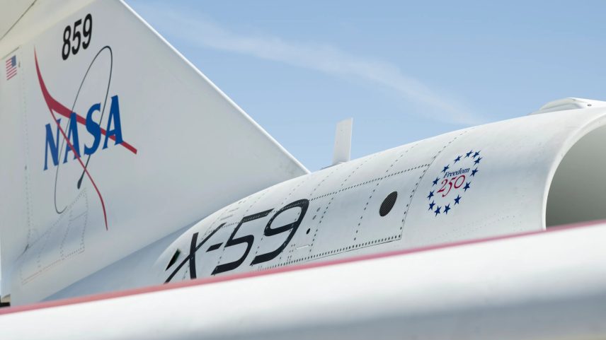 A close-up of NASA's X-59 tail showing a NASA graphic on the tail, X-59 on the side of the jet engine, and a Freedom 250 logo toward the front of the engine.