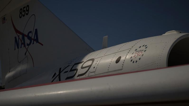 A close-up of NASA's X-59 tail showing a NASA graphic on the tail. "X-59" on the side of the jet engine, and a Freedom 250 logo toward the front of the engine.