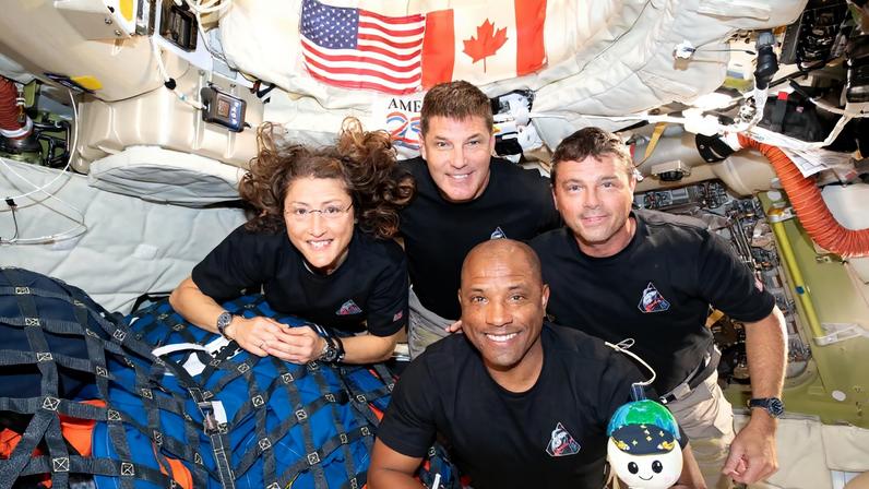 art002e013365 (April 7, 2026) – The Artemis II crew – (clockwise from left) Mission Specialist Christina Koch, Mission Specialist Jeremy Hansen, Commander Reid Wiseman, and Pilot Victor Glover – pause for a group photo with their zero gravity indicator “Rise,” inside the Orion spacecraft on their way home. Following a swing around the far side of the Moon on April 6, 2026, the crew exited the lunar sphere of influence (the point at which the Moon’s gravity has a stronger pull on Orion than the Earth’s) on April 7, and are headed back to Earth for a splashdown in the Pacific Ocean on April 10.