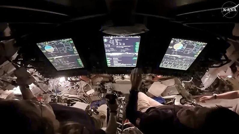 A astronauta Christina Koch (esq.) assume o controle da espaçonave durante um teste de pilotagem manual no 4º dia de voo. À direita dela estão os astronautas Jeremy Hansen e Victor Glover