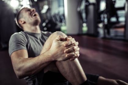 Close up of athletic man holding his knee in pain at health club.