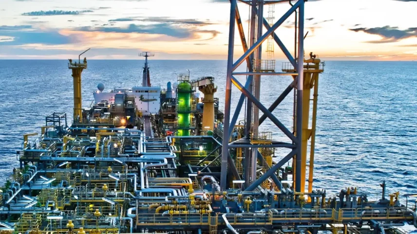 Plataforma de petróleo marítima ao pôr do sol, com maquinário complexo e mar ao fundo