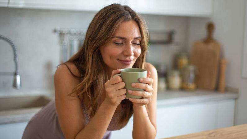 Foto colorida de mulher escorada em balcão e segurando um xícara de café - Metrópoles