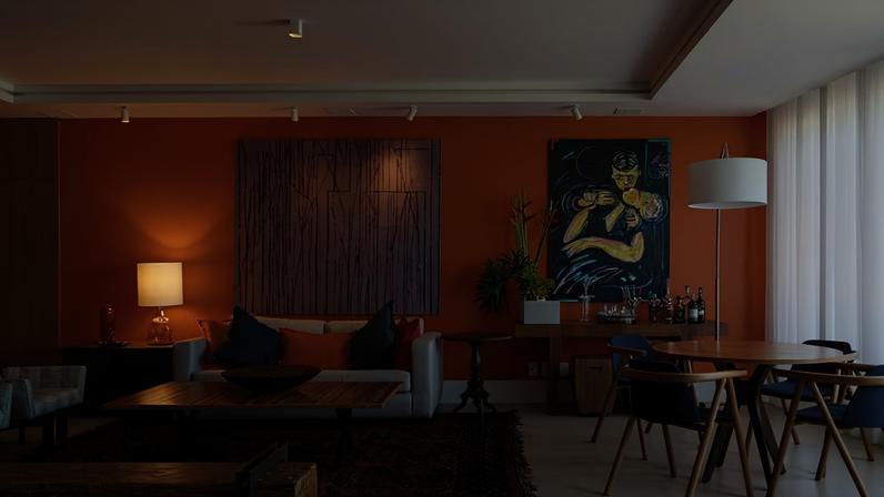 A parede pintada com a cor Laranja Revelação, da Coral, junto às telas de Gonçalo Ivo e Rubens Gerchman, cria um efeito marcante no ambiente, trazendo vitalidade e calor