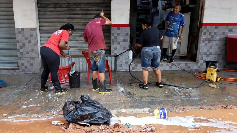 Comerciantes fazendo a limpeza após estabelecimento ser tomado por lama