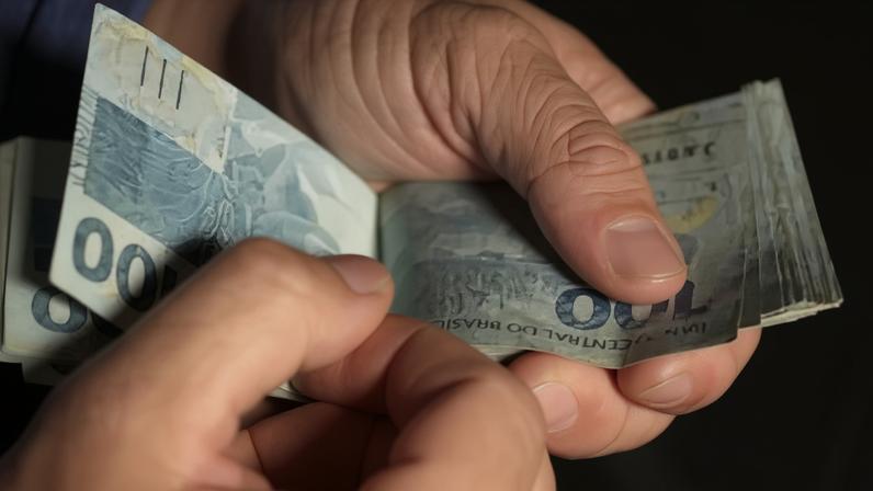 Cédula de 100 reais sendo manuseada