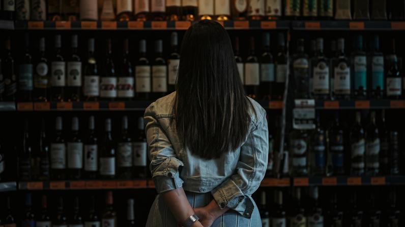 Rear view of a woman customer looking at a rack of wine in supermarket