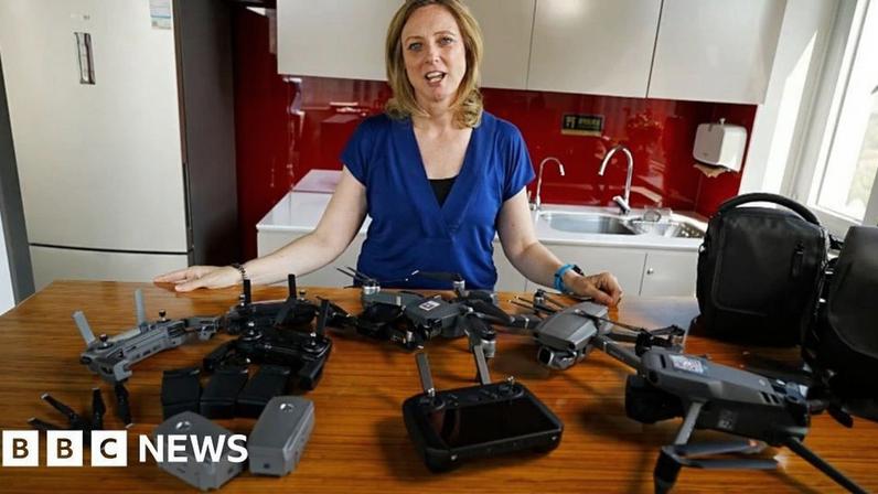 Laura Bicker, wearing a dark blue top, standing in front of a table with several drone devices on it.