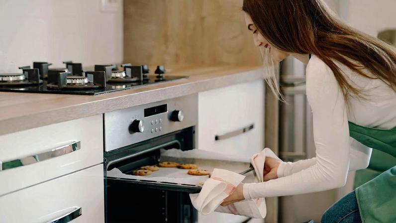 Imagem ilustrativa de uma mulher usando o forno para fazer biscoitos