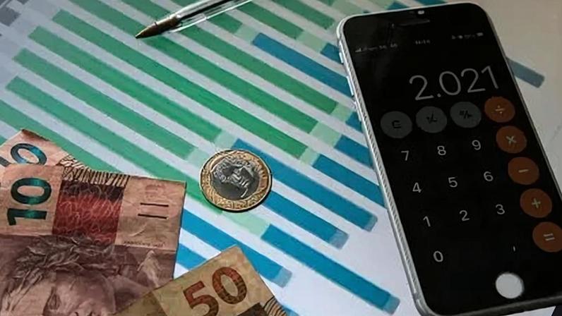 Notas e moeda de real, um celular com calculadora e uma caneta sobre o desenho de um gráfico