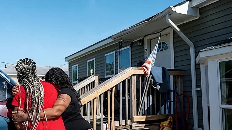 Getty Images Women hug near the entrance of a home. There's a US flag there. Some damage can be seen to the roof